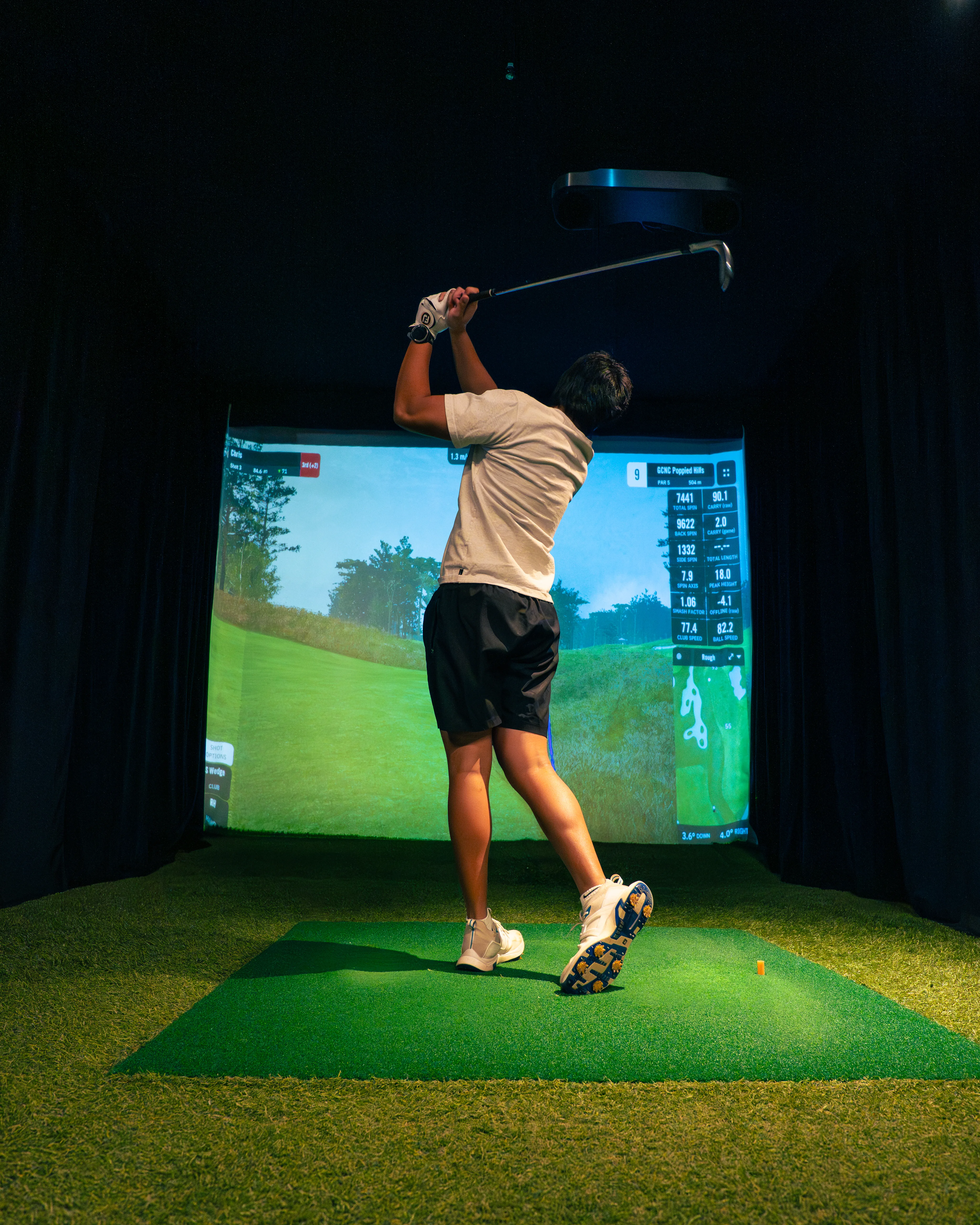 Golfer mid-swing in an indoor simulator at The Range